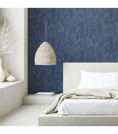 a white bed sitting under a hanging light next to a wall with blue leaves on it