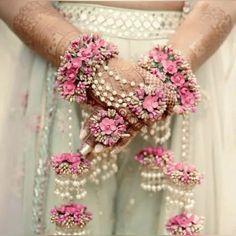 a woman in a white dress holding pink flowers and pearls on her hands, with an elaborate bracelet around her wrist