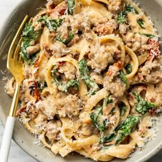 a bowl filled with pasta, meat and spinach on top of a white table