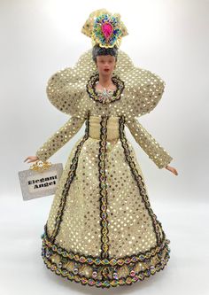 a doll is dressed in an elaborately designed dress and headpiece with a name tag