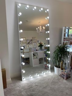 a large mirror with lights on it in a room next to a potted plant