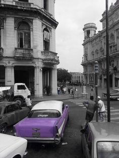 cars parked on the side of the road in front of an old building with people walking by