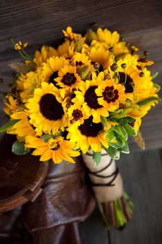 a bouquet of sunflowers in a vase on a wooden table next to a pair of brown shoes