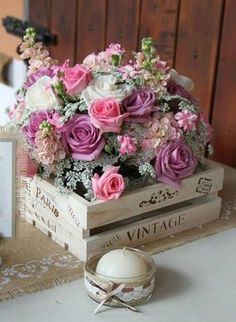 a wooden box filled with pink and white flowers on top of a table next to an egg