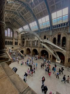 many people are walking around in an old building with high ceilings and large windows on the ceiling