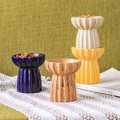 three different colored vases sitting on top of a white lace table cloth next to each other