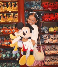 a woman holding a mickey mouse stuffed animal in front of a store filled with toys