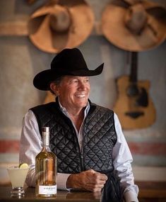 a man wearing a cowboy hat sitting at a table with a bottle of wine in front of him