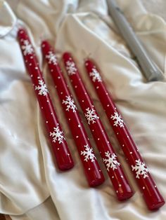 three red candles with white snowflakes on them are sitting on a satin surface