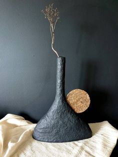 a black vase sitting on top of a white table cloth next to a wall with a plant in it