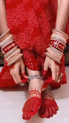 a woman in red dress with bracelets on her feet and hands holding onto something