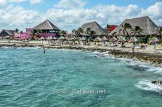 the beach is lined with thatched huts and people swimming in the blue water near the shore