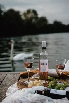 a bottle of wine and two glasses on a wooden table near water with swans in the background