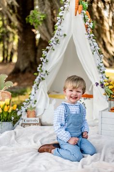 a little boy sitting on the ground in front of a teepee with carrots