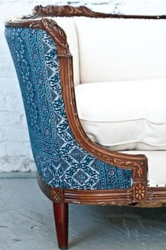 an old wooden chair with blue and white upholstered fabric on the armrests