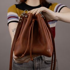 "Brown bucket bag made of genuine leather, with adjustable shoulder strap. The simple and well-made crossbody bag goes with everything and adds to your daily look with some minimalist notes. This elegant bag is perfect for holding all your daily essentials such as your phone, wallet, and keys. We offer it in 6 colors. Also, you can add personalization. This is the perfect gift for brides, wives, Mothers, Anniversaries, Weddings, or Graduation. Also, it's a nice idea for Mother's Day Gift! ♦ ♦ ♦ ♦ ♦ ♦ ♦ ♦ ♦ ♦ ♦ ♦ ♦ ♦ ♦ ♦ ♦ ♦ Our workshop makes all our products to order with great care and special attention. It's a unique handcrafted item, made of quality genuine leather. The leather texture is pleasant to touch and its remarkable and sought-after aging qualities, like the \"caramelization\" Gift Bucket Bag With Leather Handles, Gift Leather Handles Bucket Bag, Gift Bucket Satchel With Dust Bag, Leather Bucket Bag As Gift, Gift Hobo Shoulder Bag With Adjustable Strap, Hobo Shoulder Bag With Adjustable Strap As Gift, Leather Bucket Satchel As A Gift, Brown Large Capacity Bucket Bag As Gift, Gift Bucket Bag With Detachable Strap