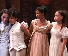 three young women standing next to each other in dresses and tuxedos on stage