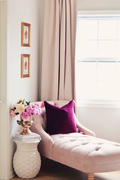 a pink chaise lounge chair in front of a window with curtains and flowers on it