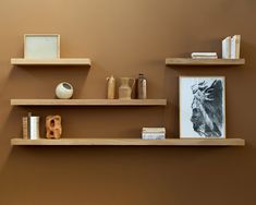 three wooden shelves with books, vases and other items on them against a brown wall