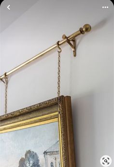 a painting hanging on the wall next to a gold frame with a golden chain around it