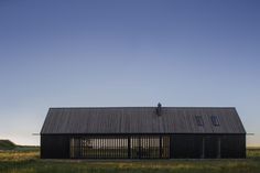 an old barn sits in the middle of a field with tall grass and blue skies