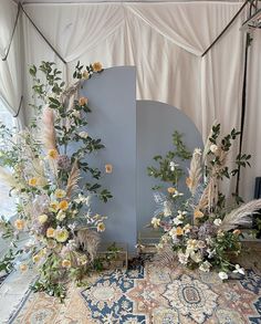 an arrangement of flowers and foliage on display in front of a mirror with white curtains