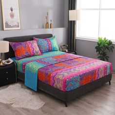 a bed with colorful bedspread and pillows in a room next to a window