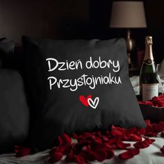 a black pillow with white writing on it next to a bottle of wine and rose petals