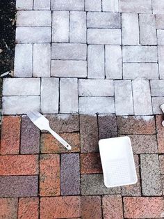 an empty white container sitting on top of a brick patio next to a spatula