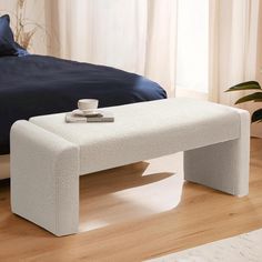 a white bench sitting on top of a hard wood floor next to a bed in a bedroom