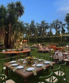 an outdoor dining area with tables and chairs set up in the grass at dusk, surrounded by palm trees