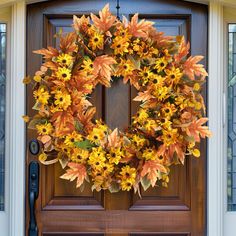 a wreath is hanging on the front door of a house with autumn leaves around it