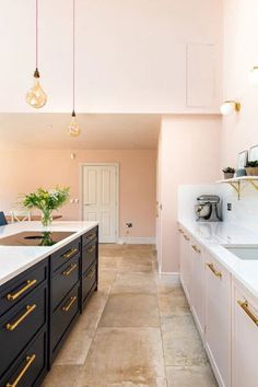 a kitchen with pink walls and white counter tops, gold trim on the cabinets and drawers