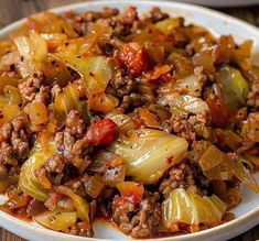 a white bowl filled with meat and vegetables on top of a wooden table next to a fork