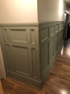 an empty room with hard wood floors and green paneling on the wall, in front of a doorway