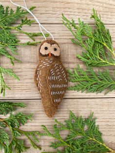 an owl ornament hanging from a tree branch on a wooden table with needles