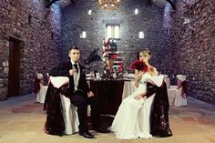 a man and woman sitting at a table in a room with stone walls, dressed in formal attire