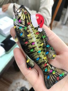 a person holding a small fish with christmas lights on it's body and wearing a santa hat