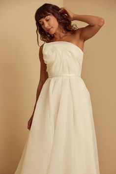 a woman in a white dress posing for the camera with her hand on her head