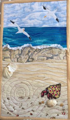 a quilted wall hanging with seashells and seagulls flying over the ocean