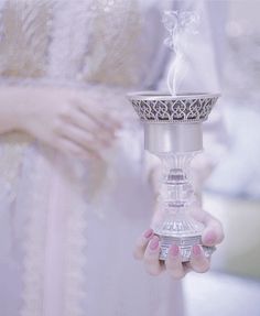 a woman in a white dress holding a silver cup with steam rising out of it