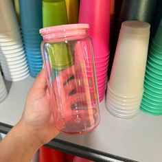 a hand holding a glass jar in front of colorful cups