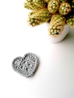 a crocheted heart sitting next to a potted plant on a table with white background