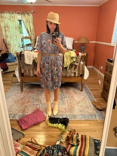 a woman taking a selfie in a bedroom with clothes on the floor and a bed behind her