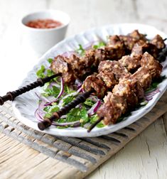 skewers of meat and vegetables on a plate with dipping sauce in the background