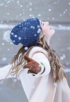 a woman with long hair wearing a blue hat and coat is throwing snow into the air