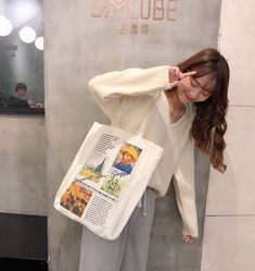 a woman holding a large white bag in front of her face while standing next to a wall