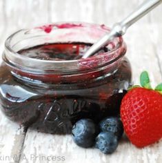 some blueberries and raspberry jam in a glass jar with a strawberry on the side