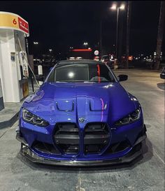 a blue sports car parked in front of a gas station with its hood up at night