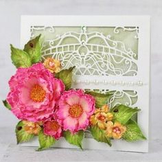 a white card with pink flowers and green leaves on the front, along with an intricate lace border